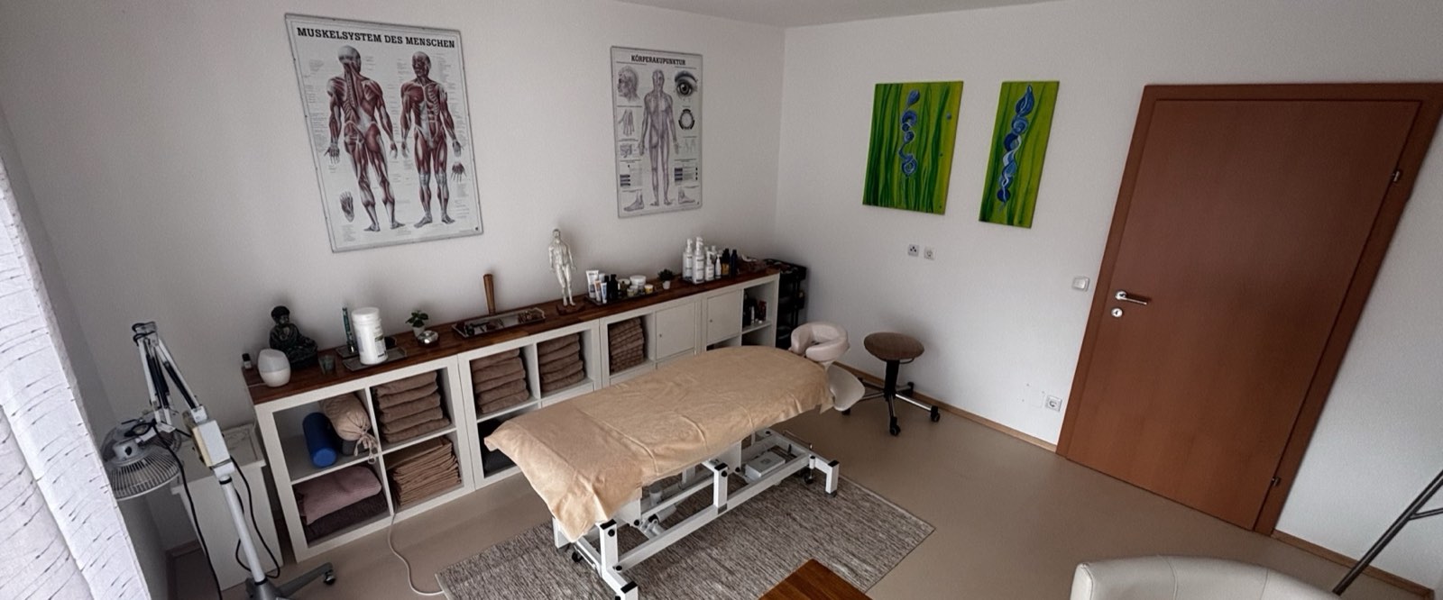 Der Behandlungsraum der Praxis mit Massageliege, Meridiantafeln und Regal