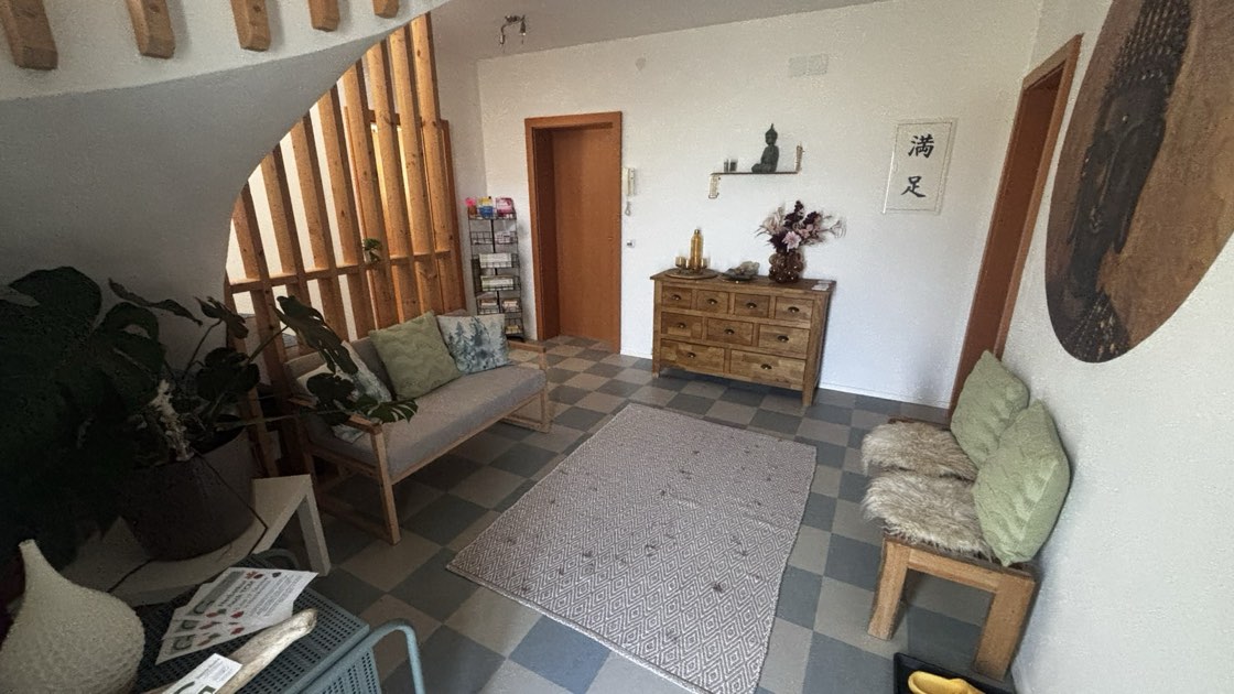 Der Wartebereich der Praxis mit Sofa, Holzkommode und Pflanzen